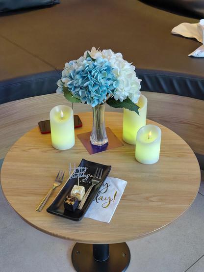 Ein kleiner Tisch ist mit drei LED-Kerzen, Kunstblumen und einem kleinen Tellerchen mir Petit Fours dekoriert. 