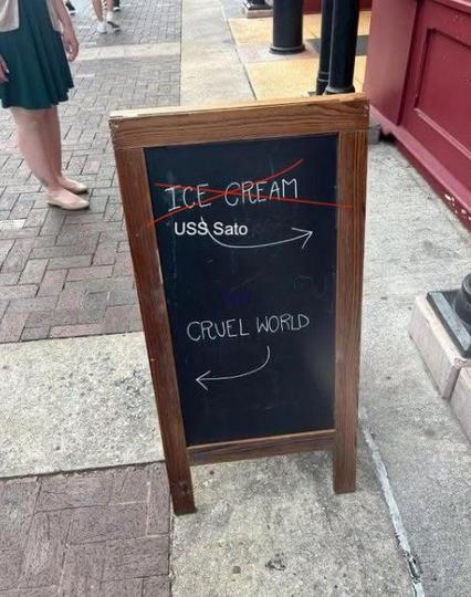 A sign in front of a shop has "Ice Cream" written on top. A arrow points from "Ice Cream" in the direction on the shop. 

Below stands "Cruel World" and a arrow points from the phrase into the direction that leads away from the shop. 

The original image has been altered with screenshot, tools. 

"Ice Cream" has been crossed out and replaced with the words "USS Sato". 